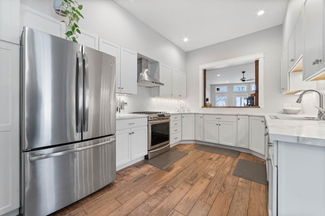 kitchen with stainless steel appliances, white cabinetry, sink, and wall chimney exhaust hood