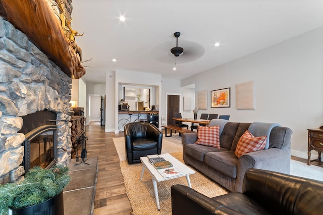 living room featuring a stone fireplace, ceiling fan, and hardwood / wood-style flooring