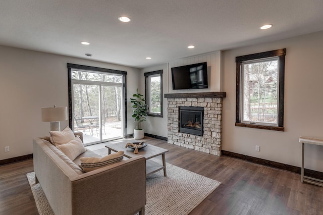 living room featuring dark wood-type flooring, a healthy amount of sunlight, and a stone fireplace