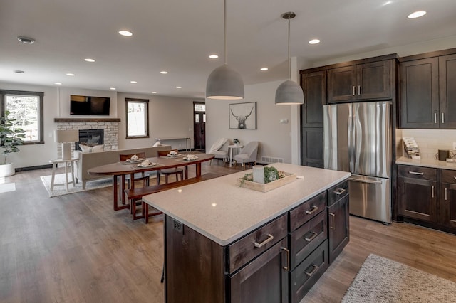 kitchen with stainless steel refrigerator, light hardwood / wood-style floors, pendant lighting, a center island, and light stone countertops