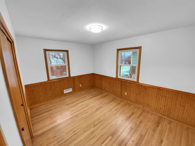 unfurnished room featuring wooden walls, light hardwood / wood-style floors, and plenty of natural light