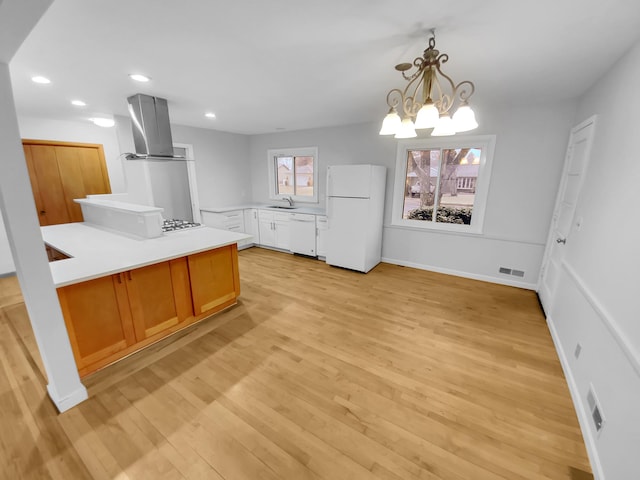 kitchen with hanging light fixtures, light hardwood / wood-style floors, wall chimney exhaust hood, white appliances, and a notable chandelier