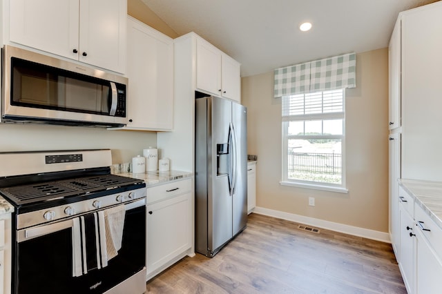 kitchen with stainless steel appliances, white cabinets, light stone countertops, and light hardwood / wood-style flooring