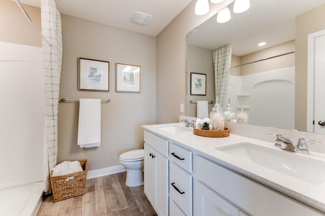 bathroom with dual sinks, vanity with extensive cabinet space, toilet, a shower, and hardwood / wood-style flooring