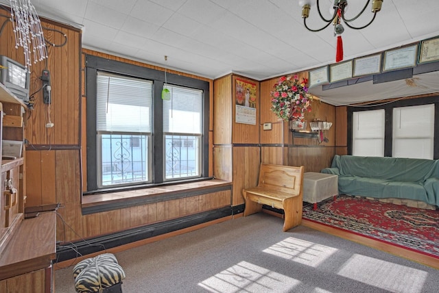 carpeted living room featuring a chandelier and wooden walls