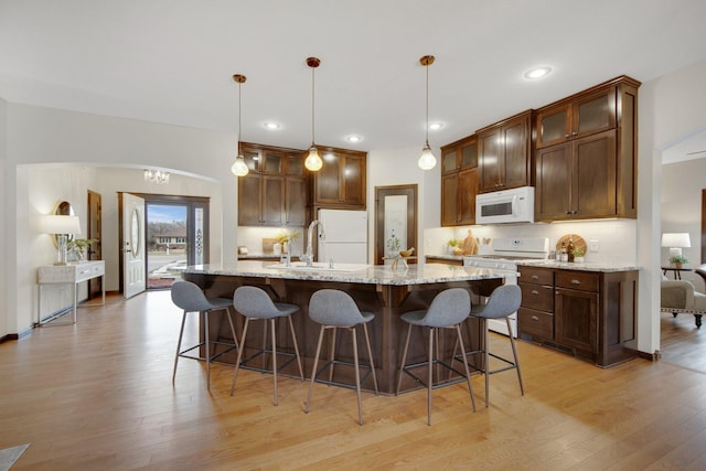 kitchen featuring light stone counters, an island with sink, decorative light fixtures, white appliances, and decorative backsplash