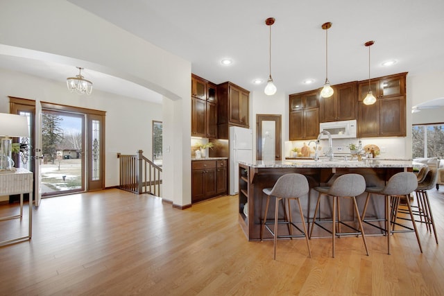 kitchen with tasteful backsplash, light stone counters, pendant lighting, white appliances, and a kitchen island