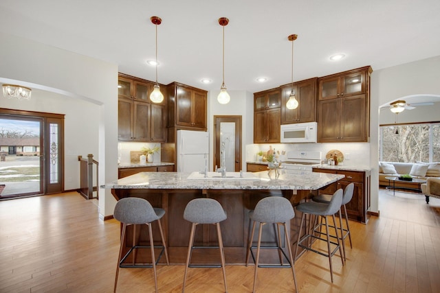 kitchen featuring light stone countertops, ceiling fan, pendant lighting, white appliances, and a kitchen island with sink