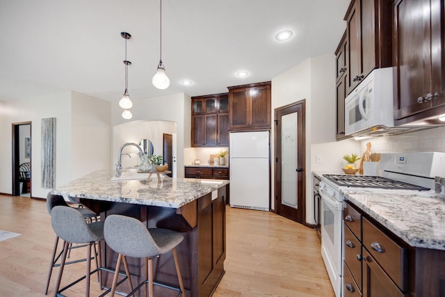 kitchen featuring tasteful backsplash, white appliances, pendant lighting, light hardwood / wood-style flooring, and an island with sink