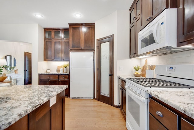 kitchen with light stone countertops, white appliances, backsplash, and light hardwood / wood-style flooring