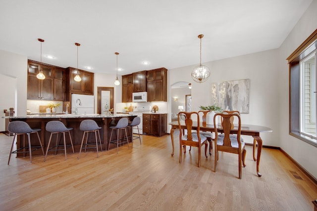 kitchen featuring light stone countertops, light wood-type flooring, white appliances, and hanging light fixtures