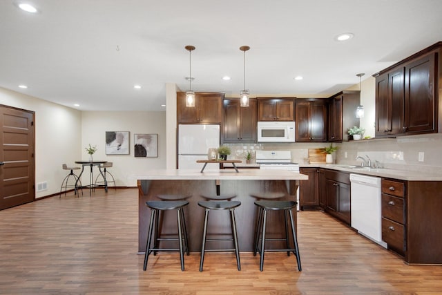 kitchen with a kitchen island, pendant lighting, white appliances, and light wood-type flooring