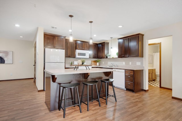 kitchen with a kitchen bar, light wood-type flooring, white appliances, pendant lighting, and a kitchen island