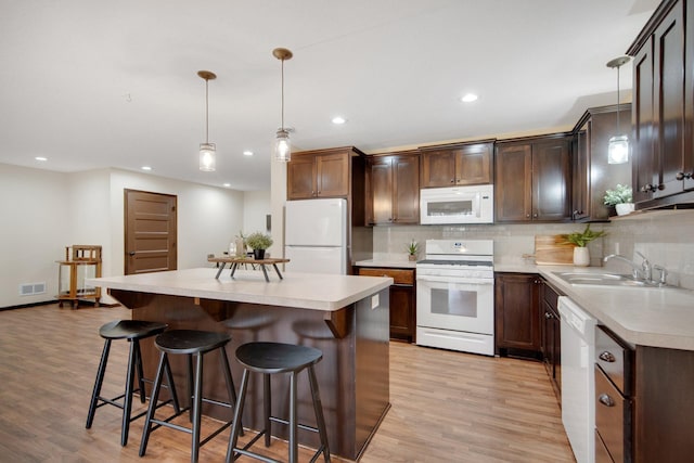 kitchen with backsplash, white appliances, sink, a kitchen island, and hanging light fixtures