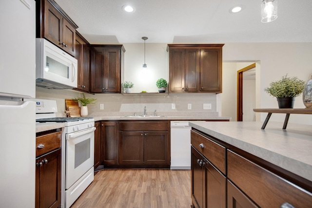 kitchen featuring light wood-type flooring, dark brown cabinetry, white appliances, sink, and hanging light fixtures