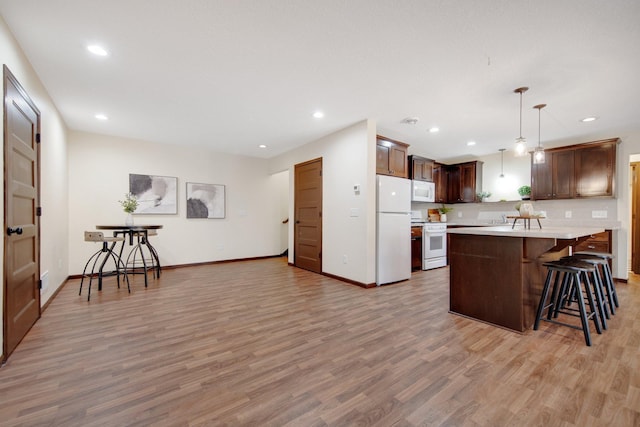 kitchen featuring a center island, white appliances, hanging light fixtures, light hardwood / wood-style floors, and a breakfast bar area