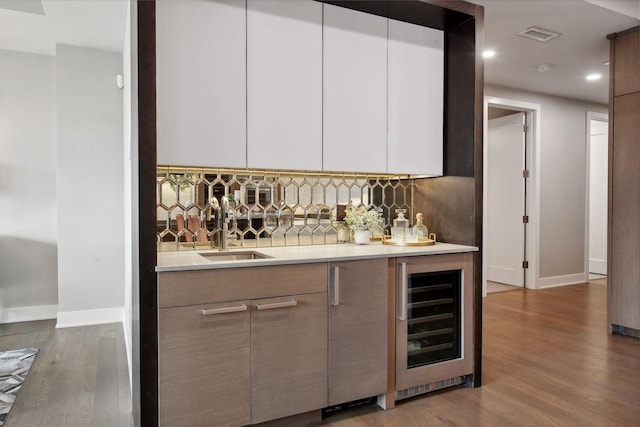 bar featuring wine cooler, sink, decorative backsplash, white cabinets, and hardwood / wood-style flooring