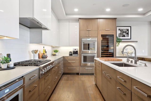 kitchen with exhaust hood, stainless steel appliances, sink, light hardwood / wood-style floors, and white cabinetry