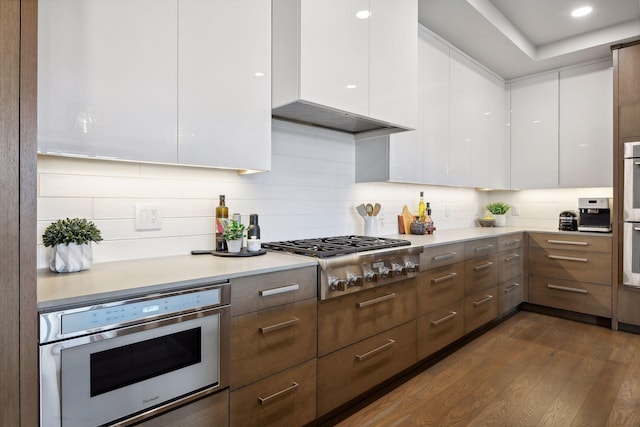 kitchen with appliances with stainless steel finishes, dark hardwood / wood-style flooring, backsplash, and white cabinets