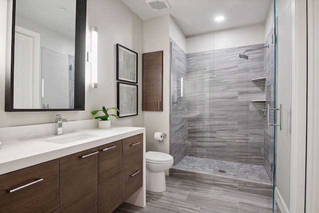 bathroom with a tile shower, vanity, and toilet