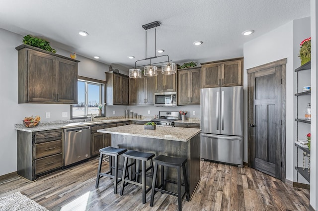 kitchen with decorative light fixtures, dark wood-type flooring, light stone counters, stainless steel appliances, and a center island