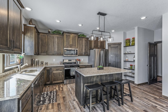 kitchen featuring stainless steel appliances, a kitchen island, decorative light fixtures, dark wood-type flooring, and light stone counters