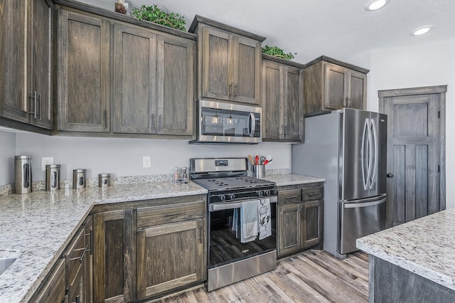 kitchen featuring light stone countertops, stainless steel appliances, light wood-type flooring, and dark brown cabinets