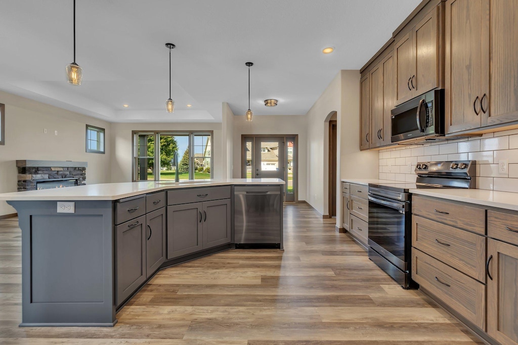 kitchen featuring appliances with stainless steel finishes, a center island, light wood-type flooring, pendant lighting, and backsplash