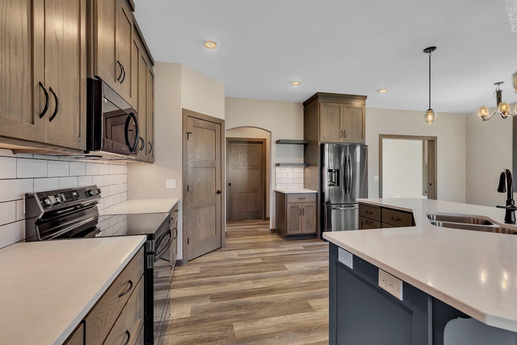 kitchen featuring stainless steel appliances, decorative light fixtures, tasteful backsplash, light hardwood / wood-style flooring, and sink