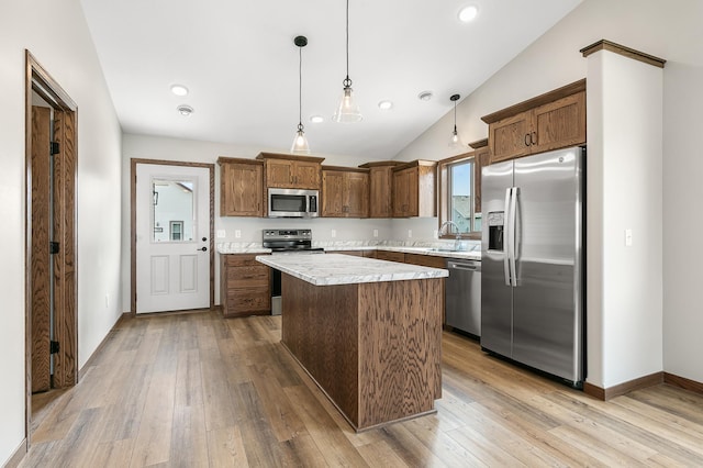 kitchen featuring decorative light fixtures, a center island, vaulted ceiling, appliances with stainless steel finishes, and light hardwood / wood-style floors