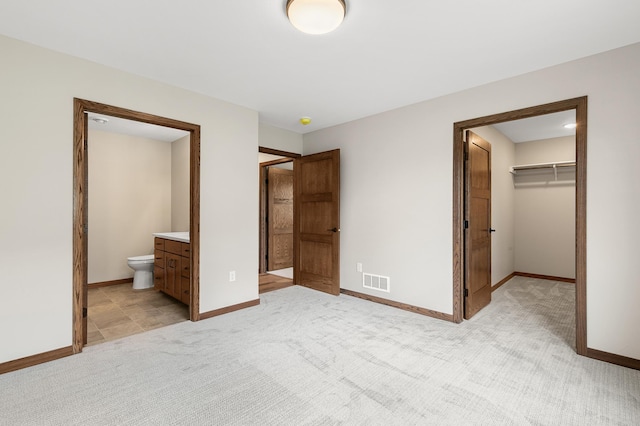 unfurnished bedroom featuring a walk in closet, light colored carpet, connected bathroom, and a closet