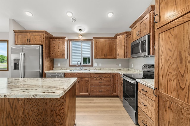 kitchen with stainless steel appliances, light stone countertops, sink, and light wood-type flooring