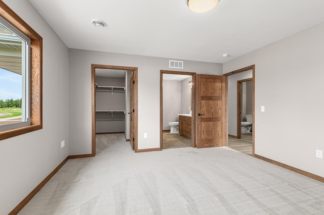 unfurnished bedroom with light colored carpet, a closet, ensuite bath, and a walk in closet