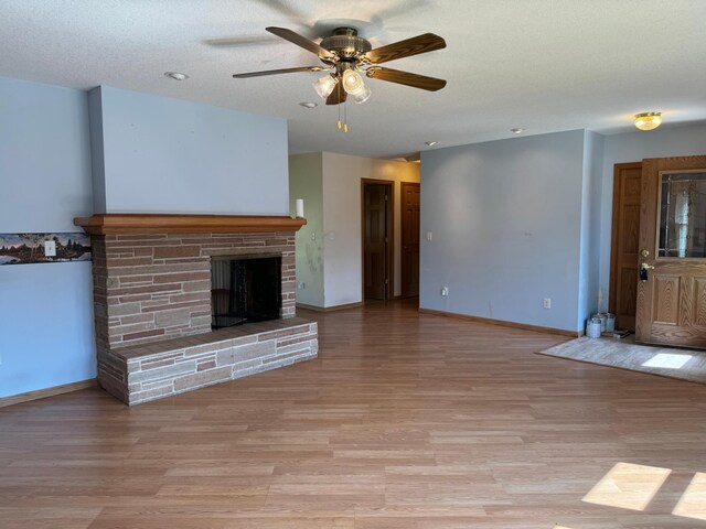 unfurnished living room featuring light wood finished floors, a fireplace with raised hearth, a textured ceiling, and baseboards