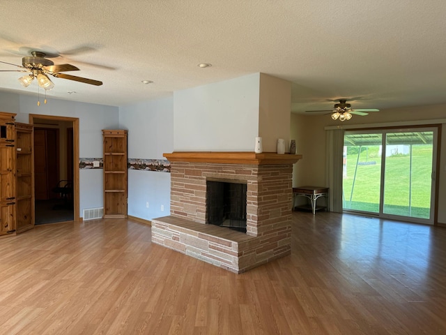 unfurnished living room with wood finished floors, visible vents, a fireplace with raised hearth, ceiling fan, and a textured ceiling