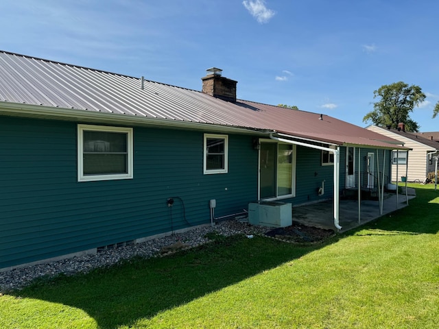 rear view of house featuring a yard, a patio area, a chimney, and metal roof