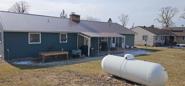 back of property with a patio area, a chimney, metal roof, and a yard