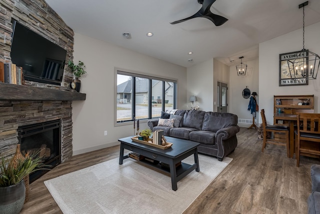 living room with ceiling fan with notable chandelier, a stone fireplace, and hardwood / wood-style flooring