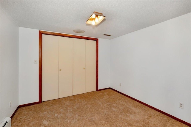 unfurnished bedroom with light colored carpet, a textured ceiling, baseboard heating, and a closet