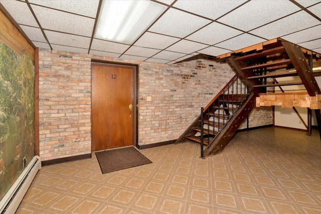 basement featuring brick wall, a baseboard heating unit, and a paneled ceiling