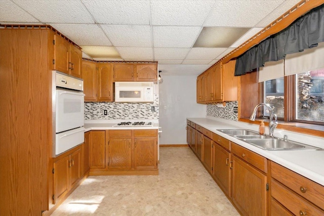 kitchen with sink, white appliances, a paneled ceiling, and decorative backsplash