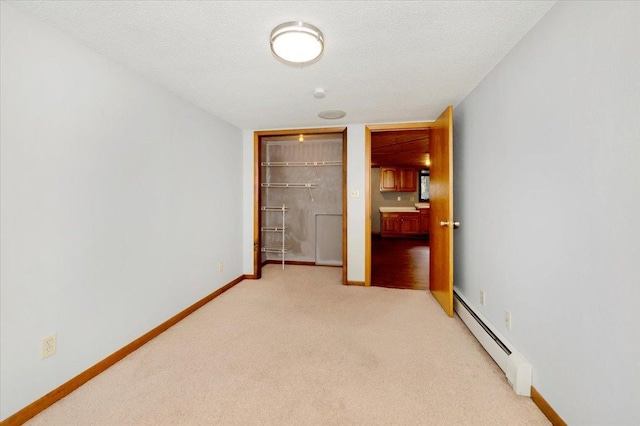 unfurnished bedroom with a closet, a textured ceiling, light carpet, and a baseboard heating unit