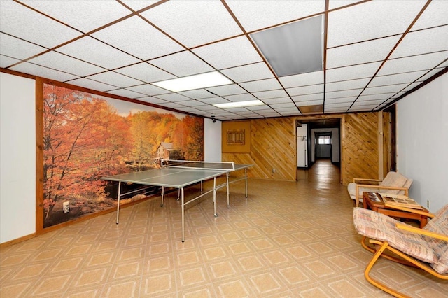 rec room with a paneled ceiling and wood walls