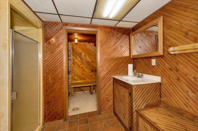 bathroom with a shower with door, tile patterned flooring, wooden walls, vanity, and a drop ceiling