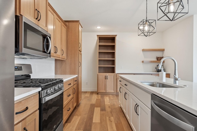 kitchen with appliances with stainless steel finishes, hanging light fixtures, sink, white cabinetry, and light hardwood / wood-style flooring