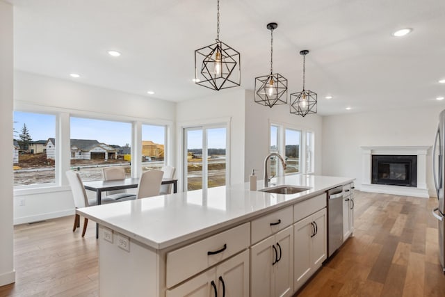 kitchen with a center island with sink, stainless steel dishwasher, light hardwood / wood-style flooring, pendant lighting, and sink