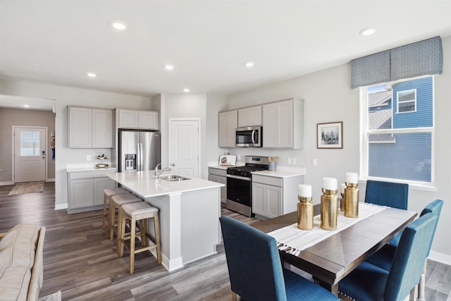 kitchen with appliances with stainless steel finishes, wood-type flooring, sink, a kitchen breakfast bar, and a kitchen island with sink