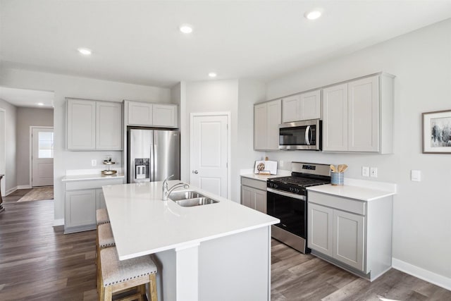 kitchen with a kitchen bar, sink, a center island with sink, appliances with stainless steel finishes, and hardwood / wood-style flooring