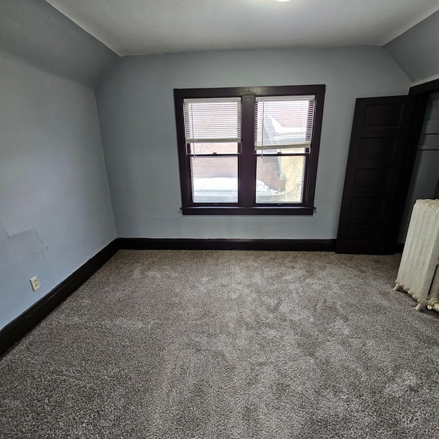 interior space featuring dark colored carpet, radiator heating unit, and vaulted ceiling