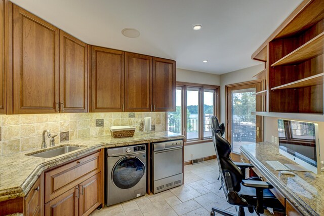 kitchen with light tile patterned floors, light stone counters, sink, decorative backsplash, and washer / dryer